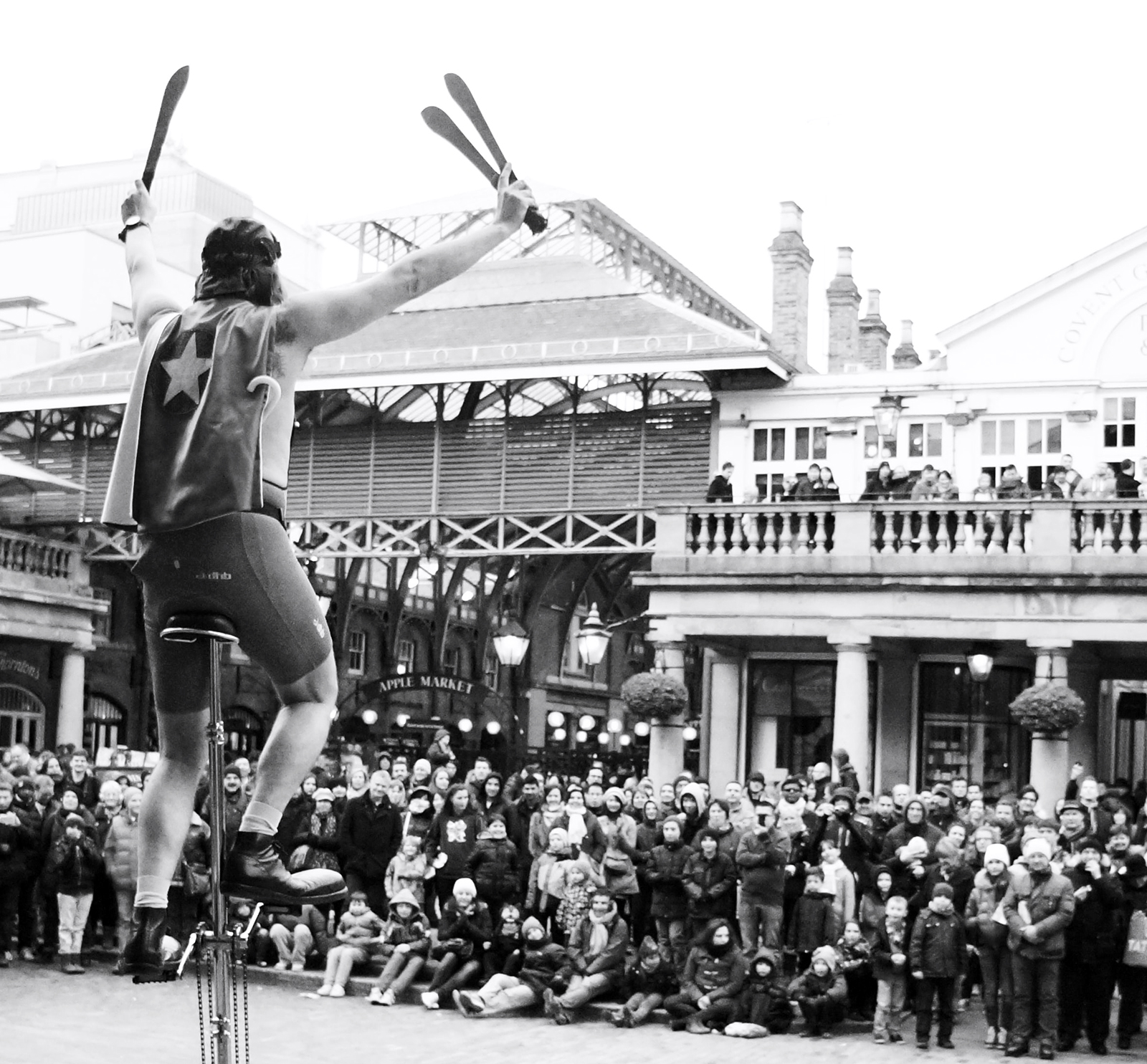 Black and white image of juggler on a unicycle in front of a crowd