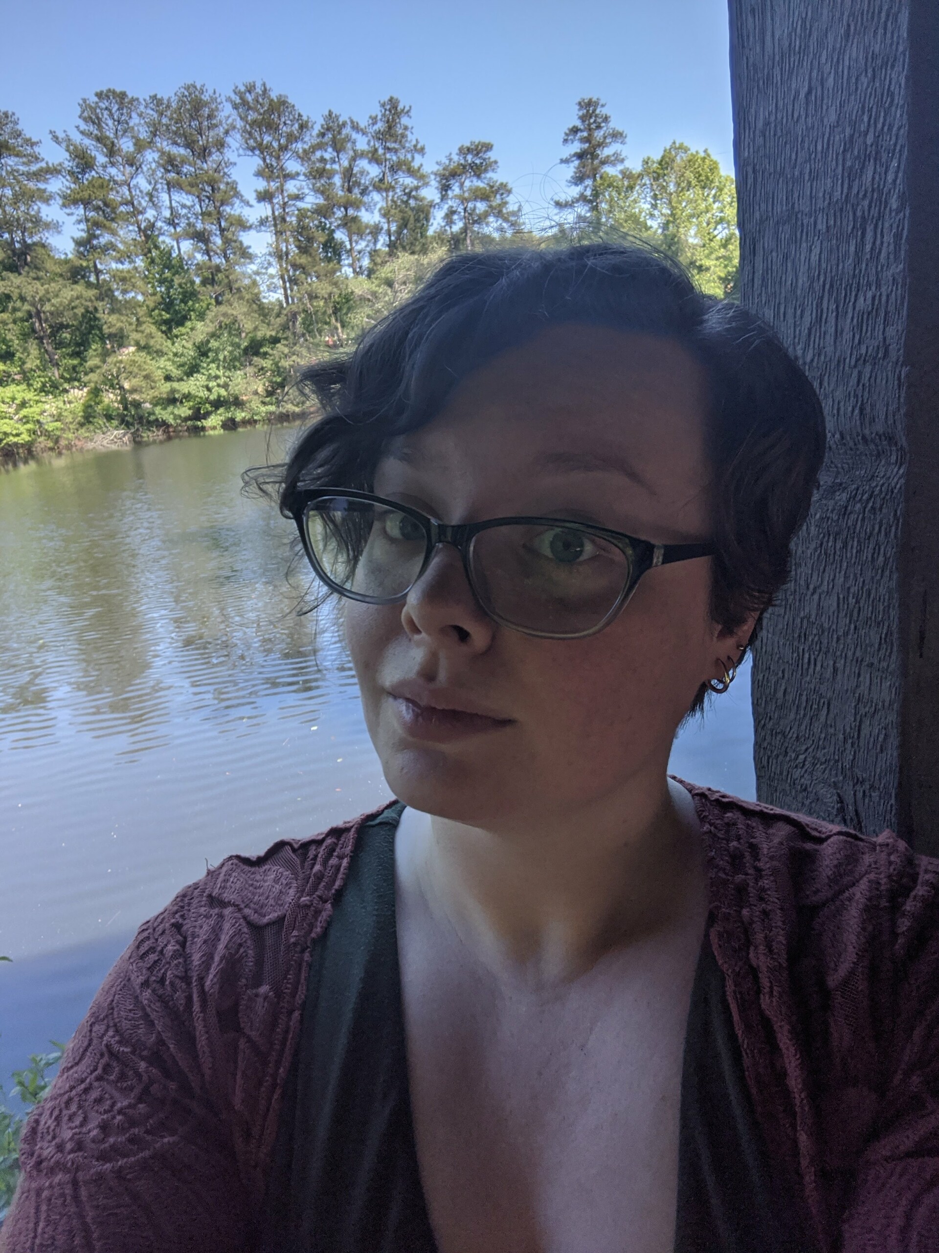 A young person with glasses and short brown hair in front of a lake.